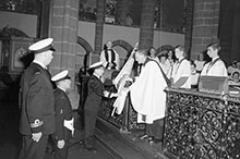 Rear-Admiral W.M. Landymore, Flag Officer Pacific Coast, presents the White Ensign for safekeeping to the Dean of Christ Church Cathedral, Victoria, British Columbia.