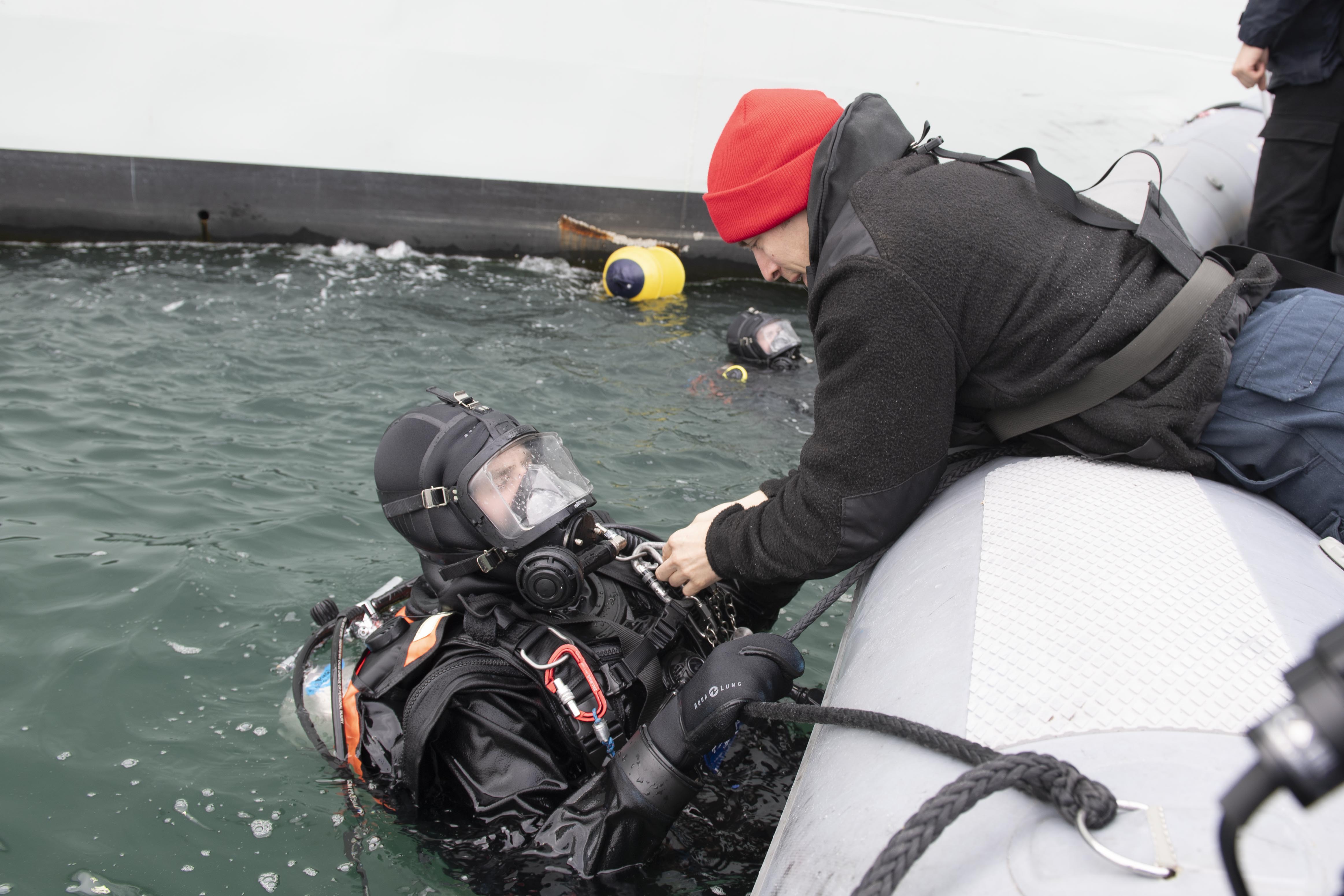 Leading Seaman (LS) Cory Taylor (right) helps LS John Kester to remove his gear at the conclusion of a diving operation at the Port of Reykjavik, Iceland